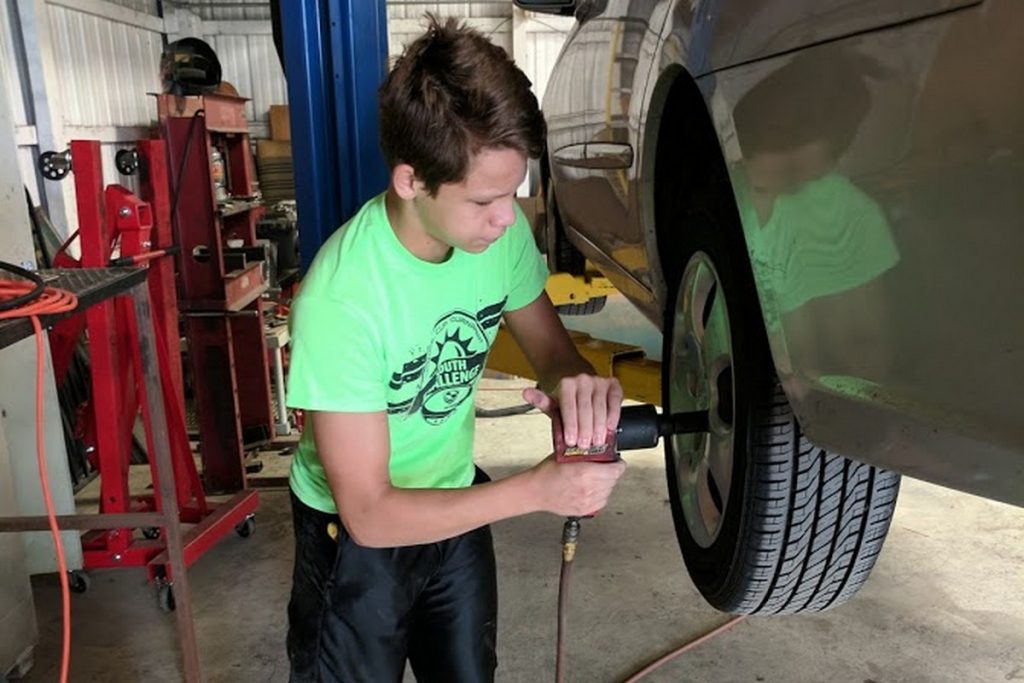 Teenage boy using an impact wrench to remove a lug nut from a car on a lift