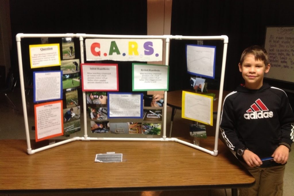 Boy stands next to science fair display - made of PVC pipe