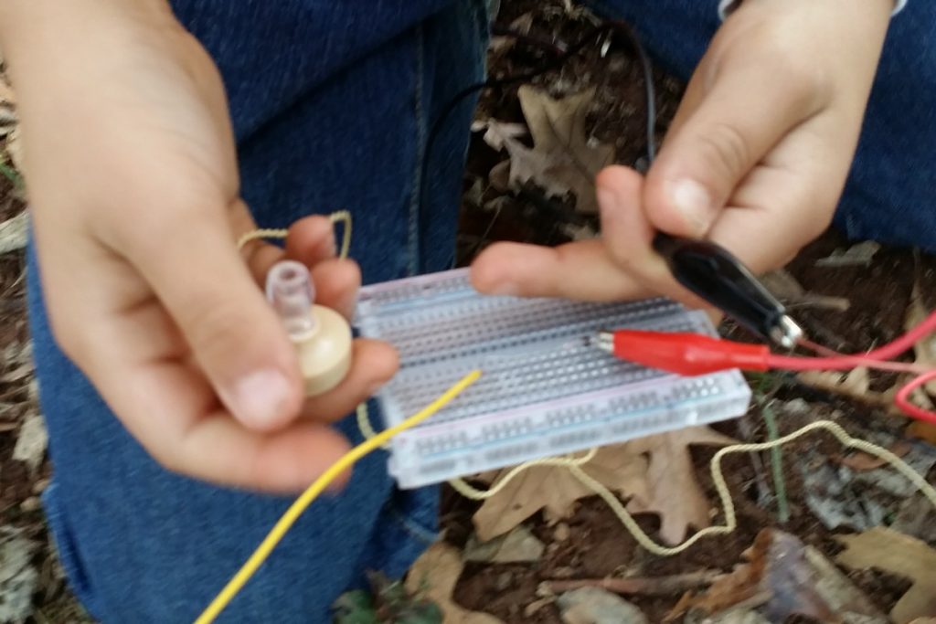 Child holding circuit breadboard with very few wires and an earpiece