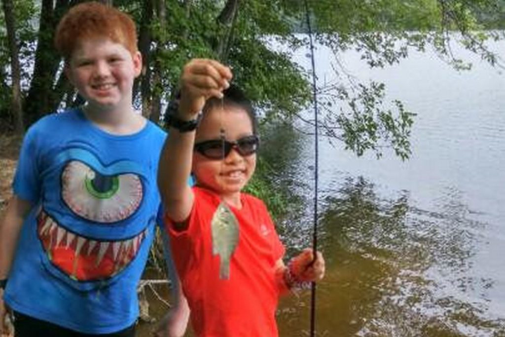 Two kids holding a rod and a showing small fish on the line