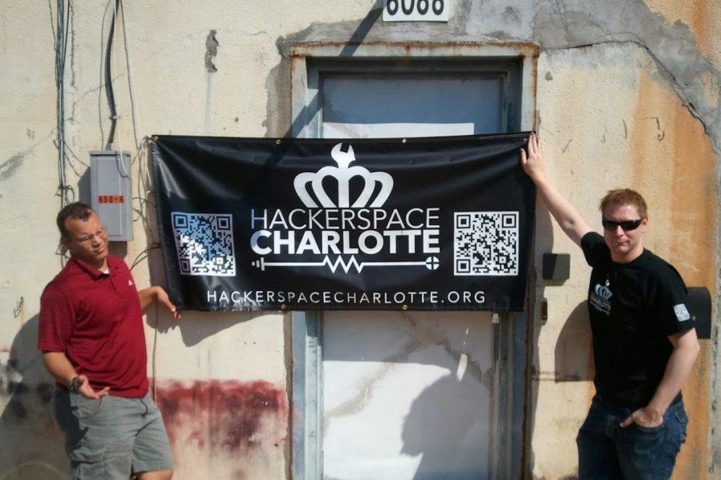 Quincy and Max standing at the entrance to Freeside Atlanta holding the Hackerspace Charlotte banner over the door