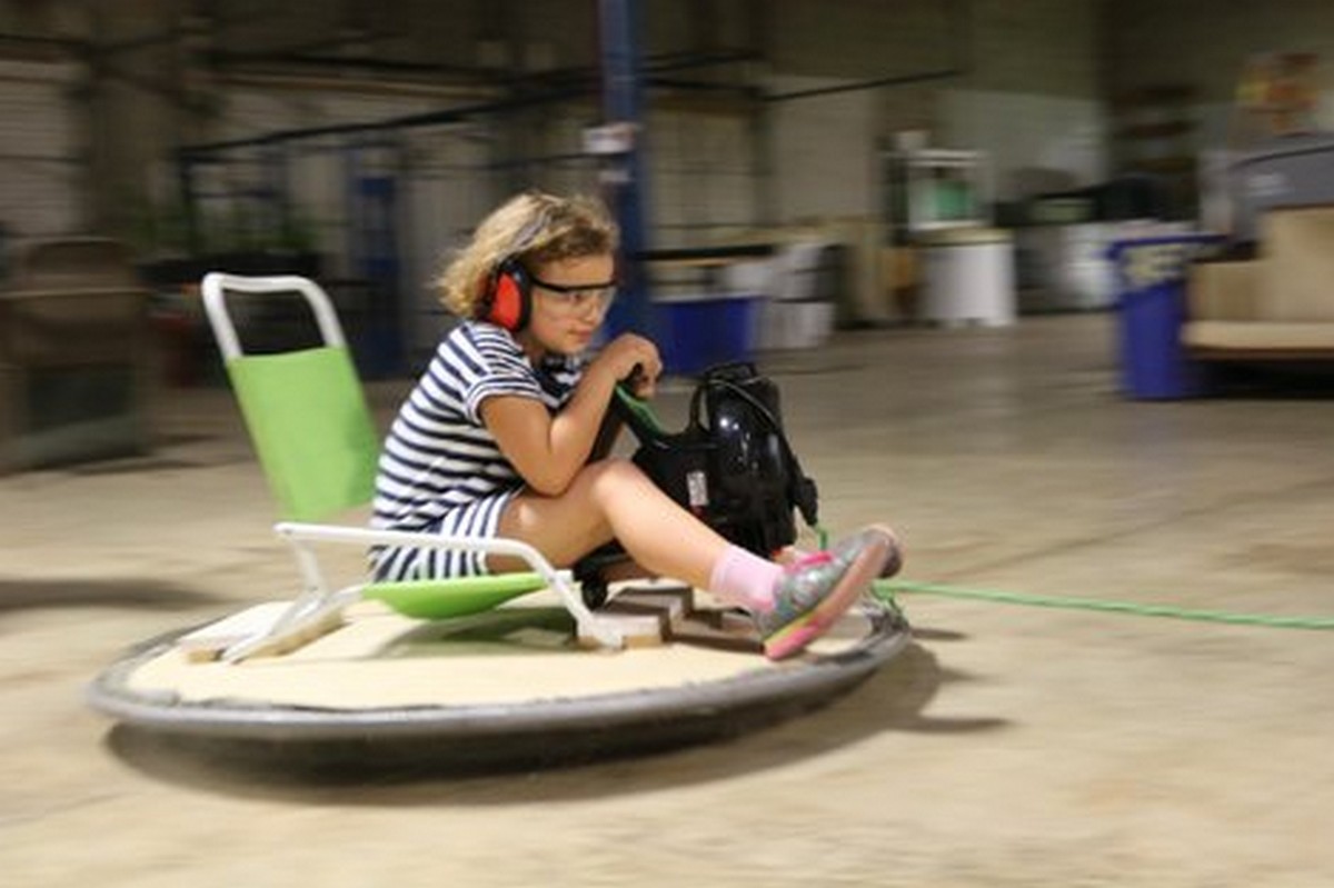 Girl on riding hover board sitting lawn chair holding leaf blow down with speed motion blur