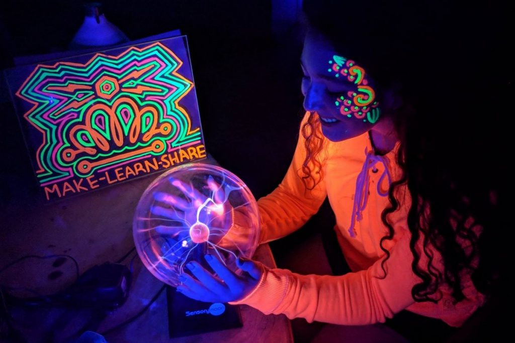 Girl with glow in the dark paints on her face holding a plasma sphere lightning ball