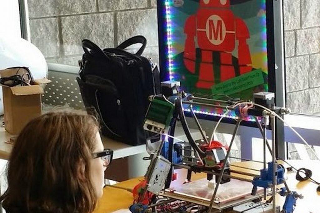 Child sits watching 3D printer in the Library