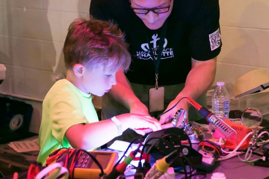 Child sitting at a soldering station with adult looking on