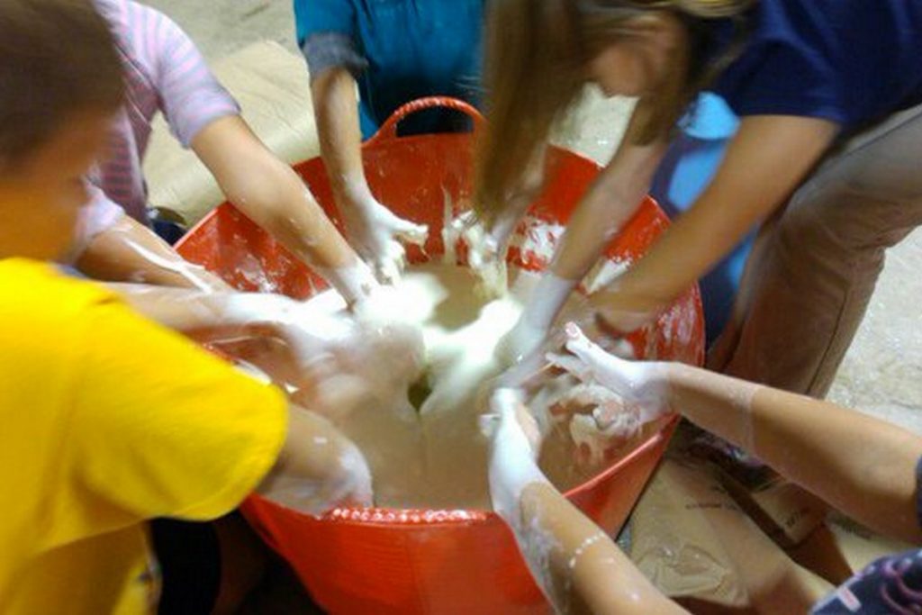 5 kids mixing conrstarch and water by hand in a 15 gallon bucket