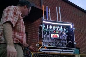 Roadie case with PVC, wires, lights, and a small screen with a raspberry drawing displayed. The tubes go out the top with paper rockets on top