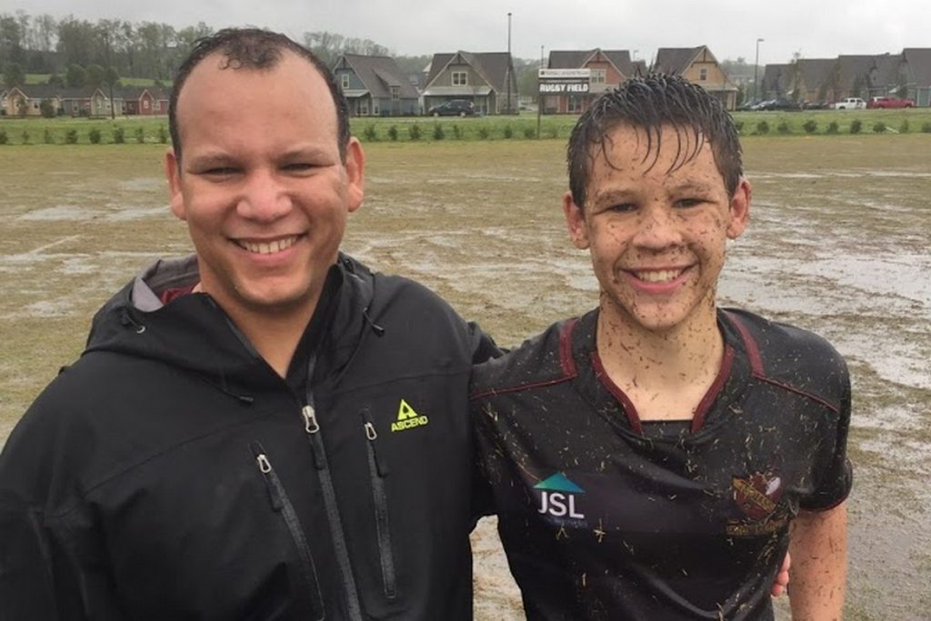 Teenage boy covered in grass and mud standing next to father