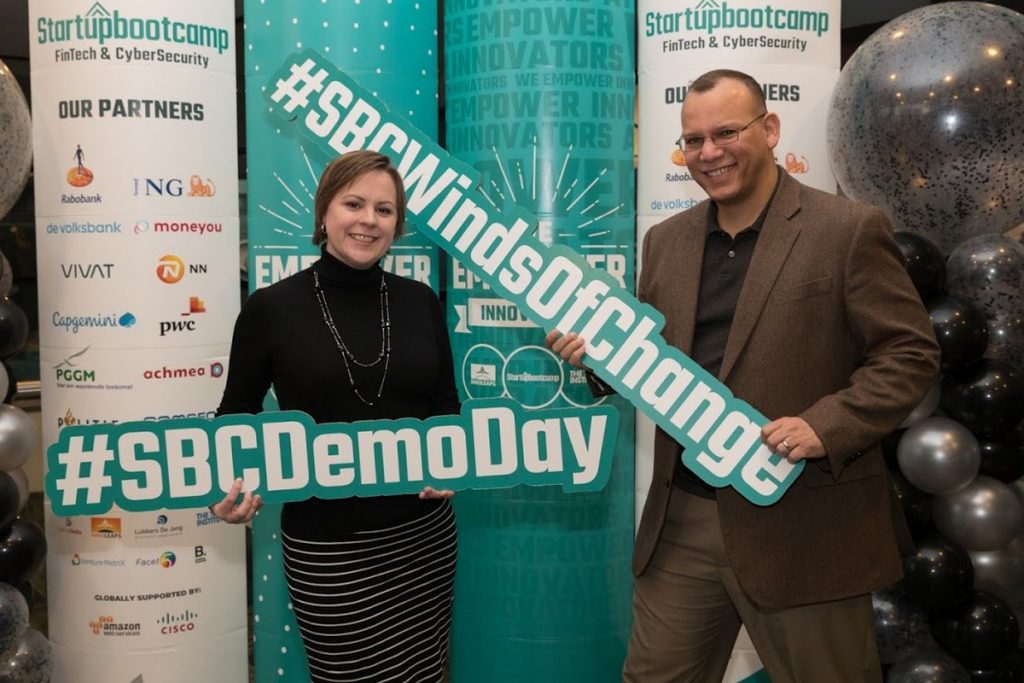 Man and woman holding word signs that read @SBCDemoDay, and #SBCWindsOfChange