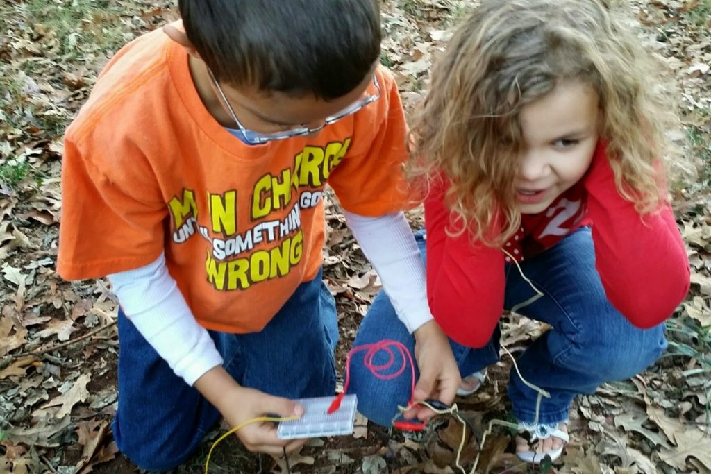 Boy and girl crouch low to ground to listen to very primitive radio