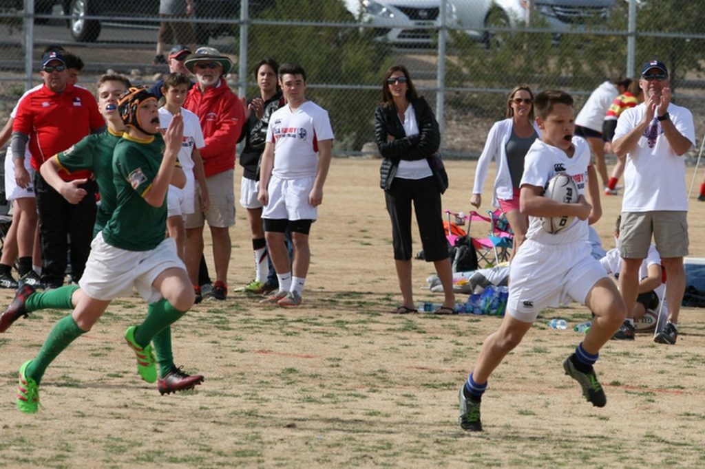 Kids playing rugby - white player running with ball with green player in pursuit